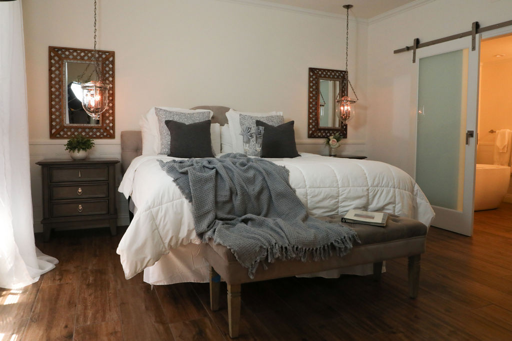 A large bed with white bedding and gray throw blanket in a room with wood floors and two mirrors on the wall.